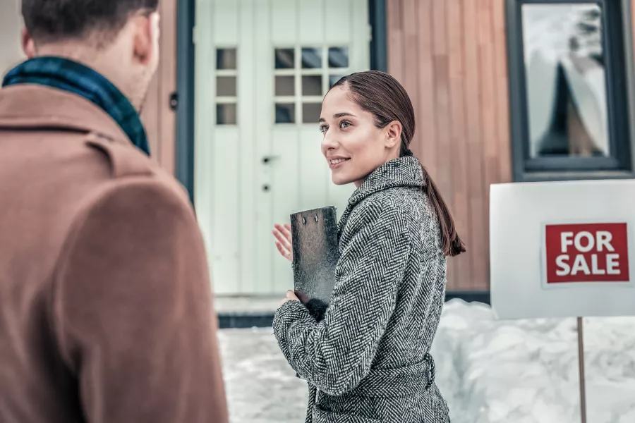 An agent meets with her clients outside a home for sale in the winter snow.