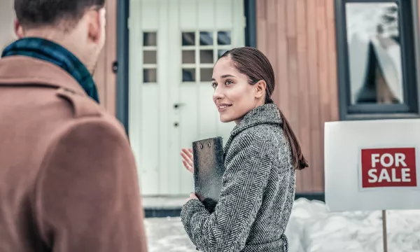 An agent meets with her clients outside a home for sale in the winter snow.